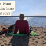 Blonde Frau sitzt an Seestrand und schaut in die Ferne, Ansicht von hinten