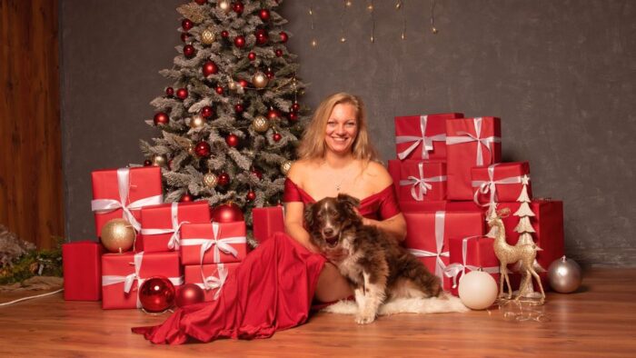 Frau in rotem Kleid mit ihrem braunem Hund vor weihnachtlicher Deko im Fotostudio